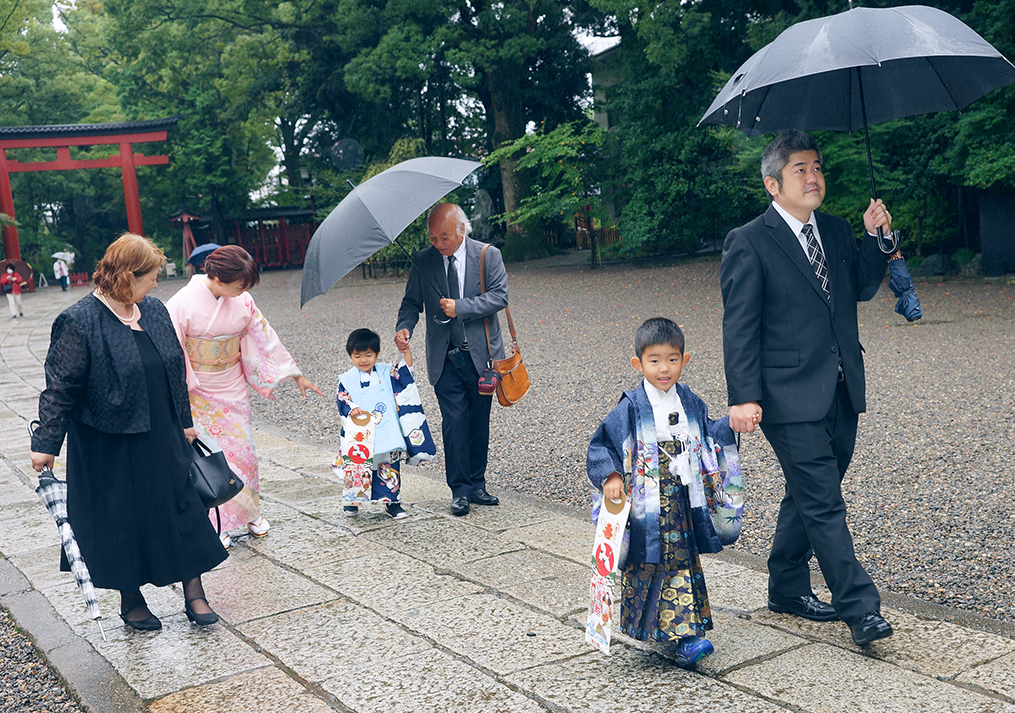 雨の中傘をさして参道を歩く家族