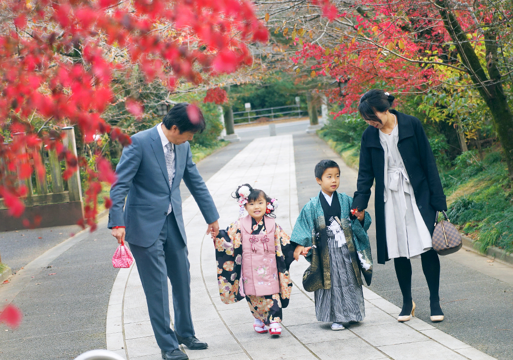 紅葉の下の参道を歩く家族