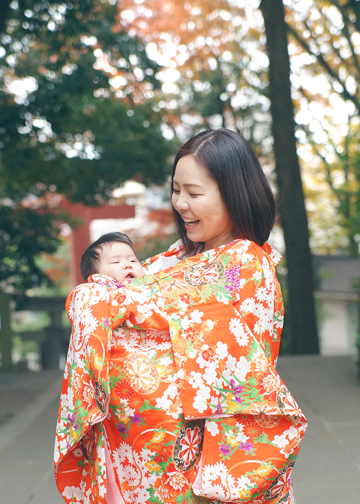 オレンジ色の祝い着を掛けて赤ちゃんを抱っこするママ