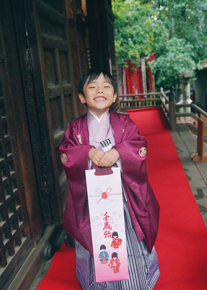 七五三出張撮影で代々木八幡宮の本殿で千歳飴を持ってはしゃぐ男の子の写真