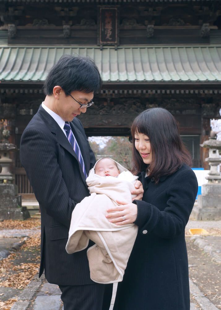 正中山法華経寺の門の下でお宮参りの赤ちゃんを抱っこするパパ