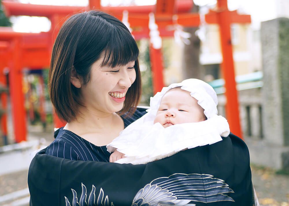 お宮参りで黒い祝い着をかけて赤ちゃんを抱っこするママ