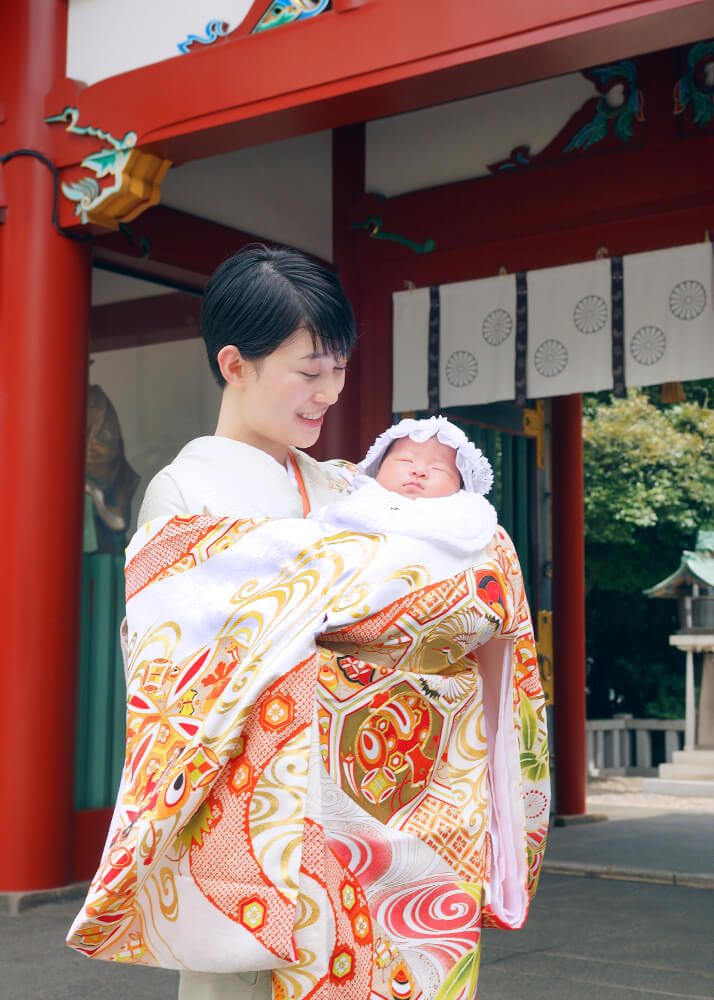 赤坂日枝神社でのお宮参り出張撮影で白とオレンジ色の祝い着をかけて赤ちゃんを抱っこするママ