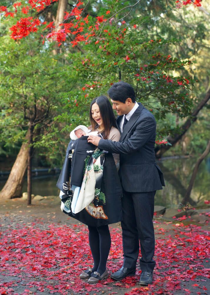 お宮参りの出張撮影で大宮氷川神社の紅葉の下で赤ちゃんを抱っこするママとパパ