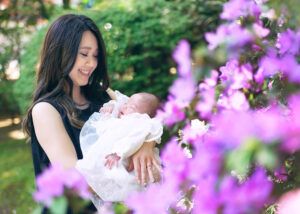 お宮参りの出張撮影で大宮氷川神社の境内の花の前で赤ちゃんを抱っこするママ