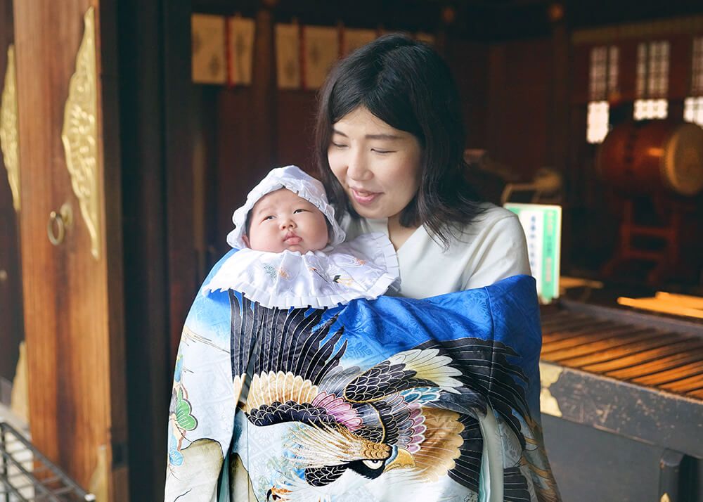 松陰神社|お宮参り・七五三・お食い初め写真 10 お宮参り出張撮影で世田谷区松陰神社の本殿の前で赤ちゃんを抱っこするママの写真