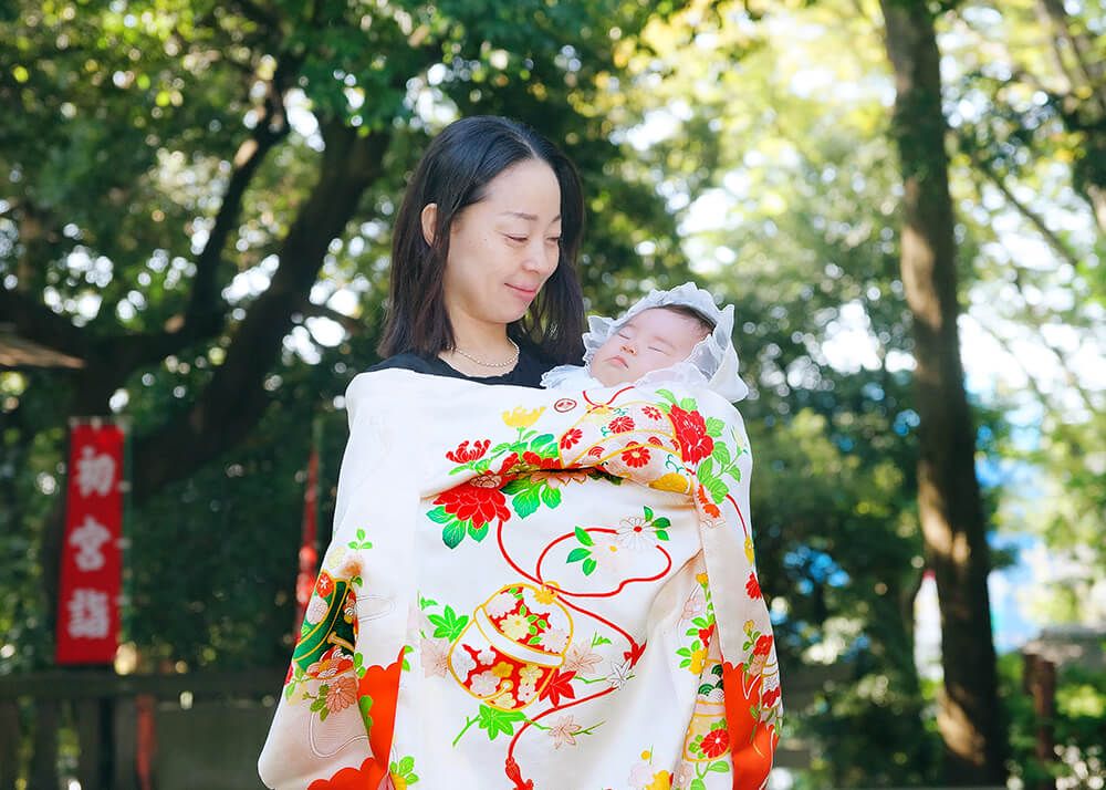 世田谷八幡宮でのお宮参り出張撮影で白とオレン色の祝い着をかけて赤ちゃんを抱っこするママ