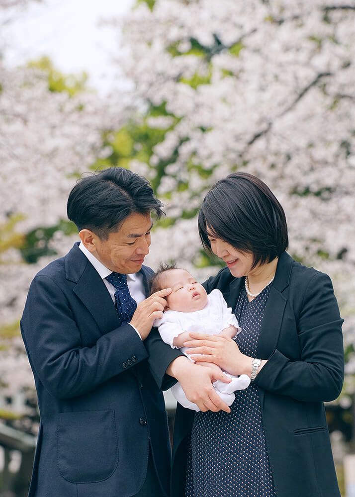 お宮参り出張撮影で世田谷八幡宮の桜の前で赤ちゃんを抱っこするママ