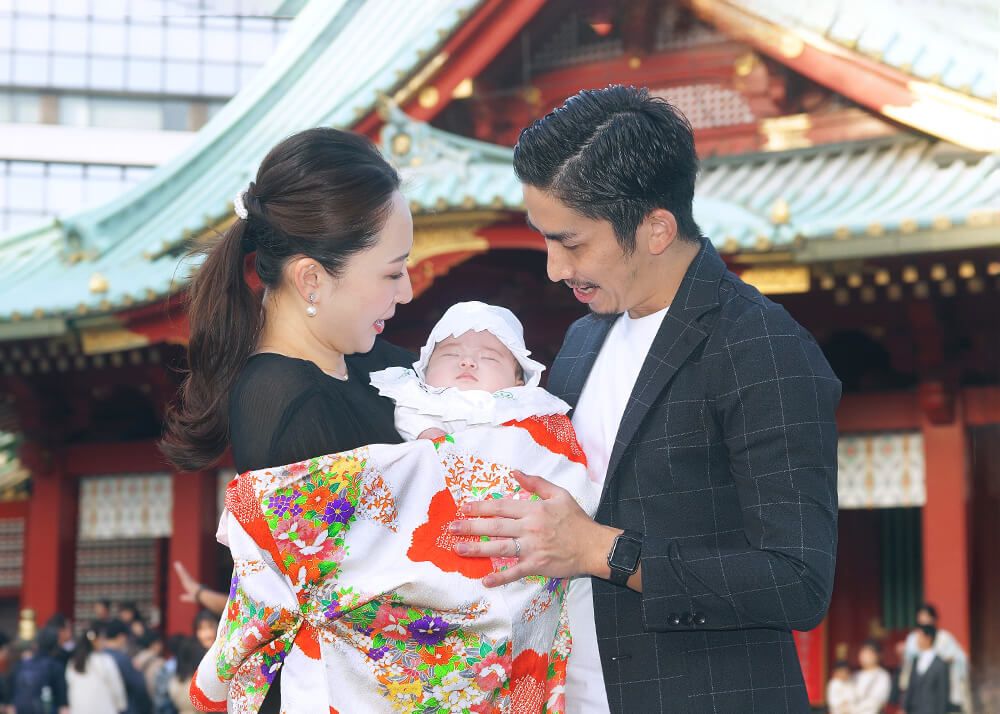 神田明神|安心!お宮参り・七五三・お食い初め写真 16 お宮参り出張撮影で神田明神の本殿前で赤ちゃんを抱っこするママとパパの写真