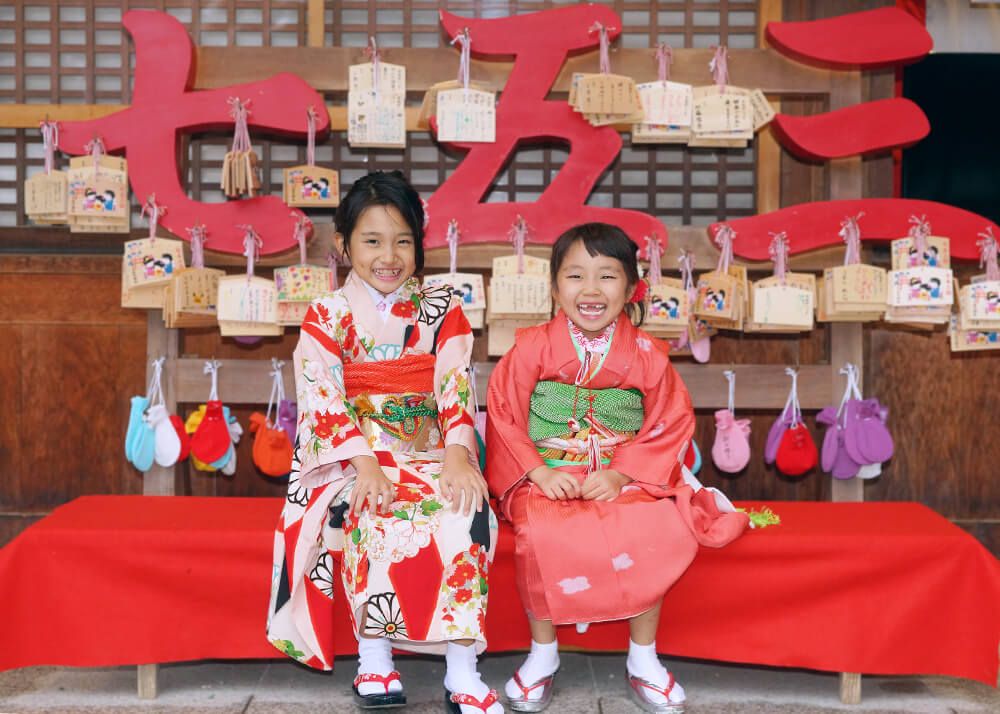 七五三ロケーションフォト-おすすめの時期|大宮氷川神社 15 七五三出張撮影で大宮氷川神社の絵馬の前に座る姉妹の写真
