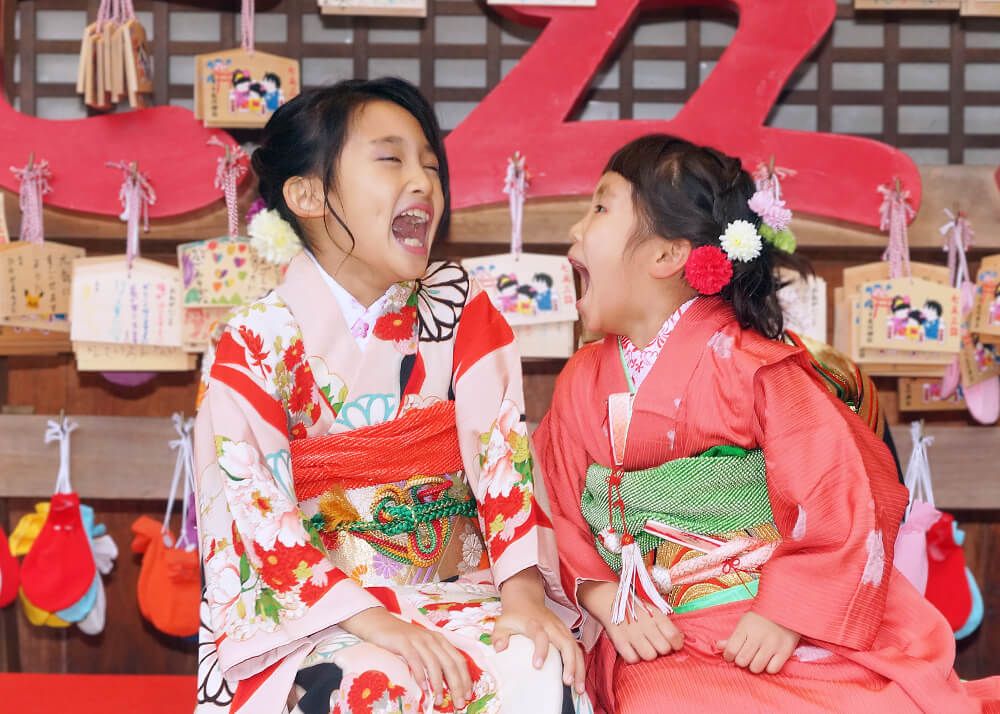 七五三ロケーションフォト-おすすめの時期|大宮氷川神社 16 七五三出張撮影で大宮氷川神社の絵馬の前ではしゃぐ姉妹の写真