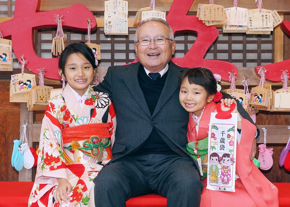 七五三ロケーションフォト-おすすめの時期|大宮氷川神社 18 七五三ロケーションフォトで大宮氷川神社の絵馬の前で姉妹と祖父の写真