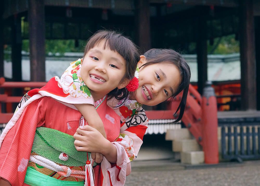 笑顔のお姉ちゃん 七五三ロケーションフォトで大宮氷川神社の楼門の前で抱き合う姉妹の写真