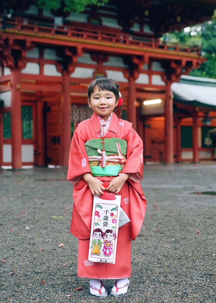 七五三ロケーションフォト-おすすめの時期|大宮氷川神社 9 七五三ロケーションフォトで大宮氷川神社の楼門の前で千歳飴を持った女の子の写真