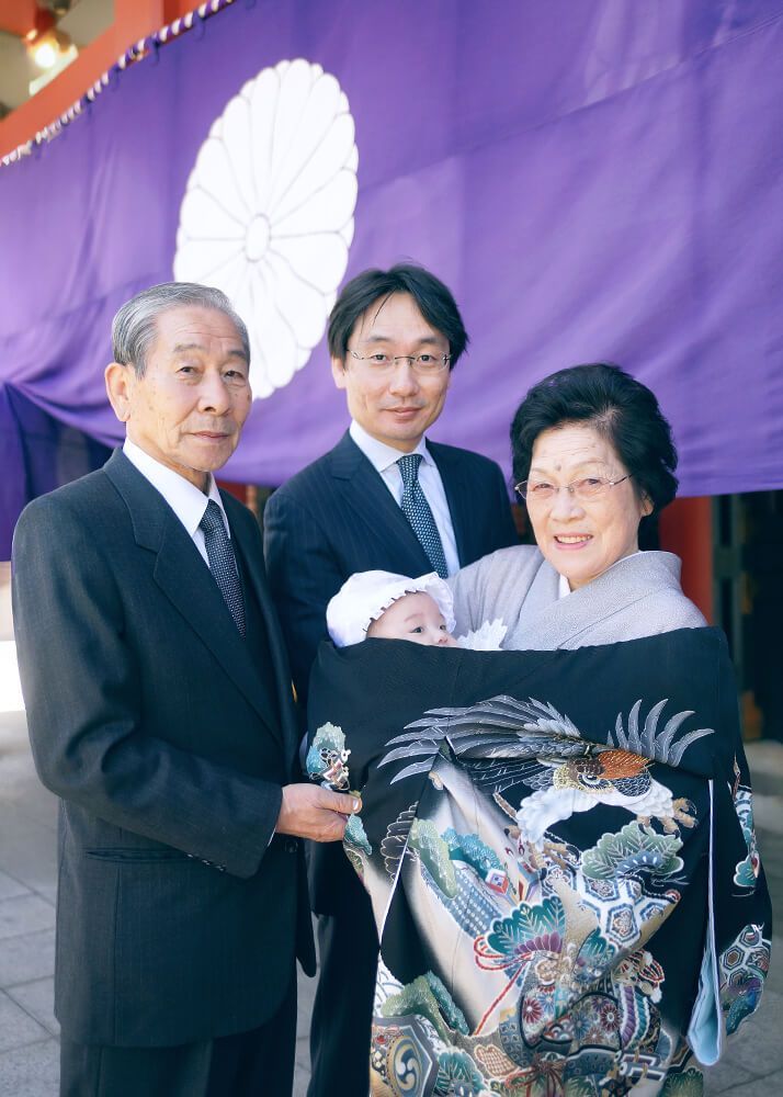 お宮参り・お食い初めロケーションフォト|赤坂日枝神社→芝とうふ屋うかい 6 赤坂日枝神社でのお宮参りロケーションフォトで本殿の前で赤ちゃんを抱っこする祖父母の写真